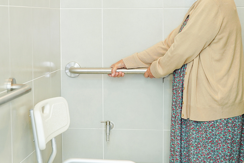 An elderly woman uses a bar in the shower for extra safety.