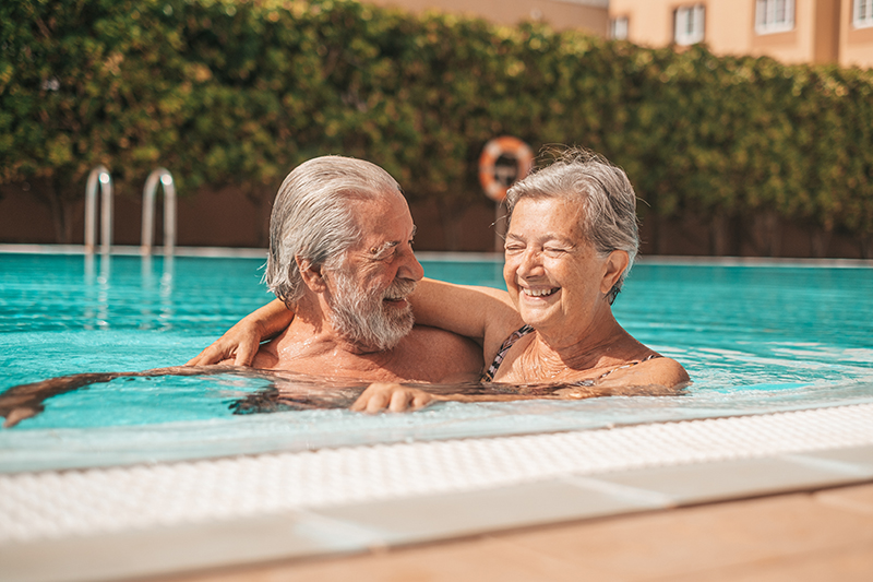 Two older adults enjoy swimming and wonder how very hot weather affects the elderly.