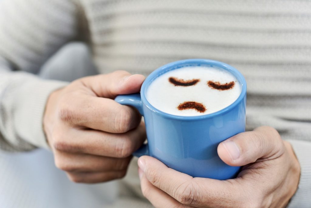 Sad face is coffee cup with older adult hands holding the cup