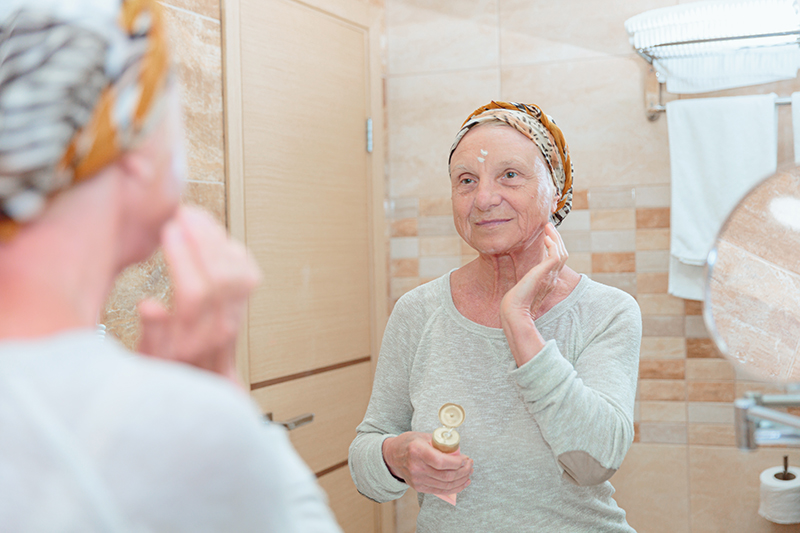 senior woman applying cream to her face with supplies nearby