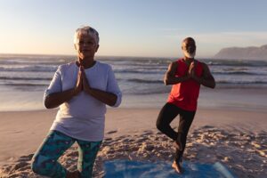 Importance of Balance As We Age. Senior woman and mad do yoga on the beach.