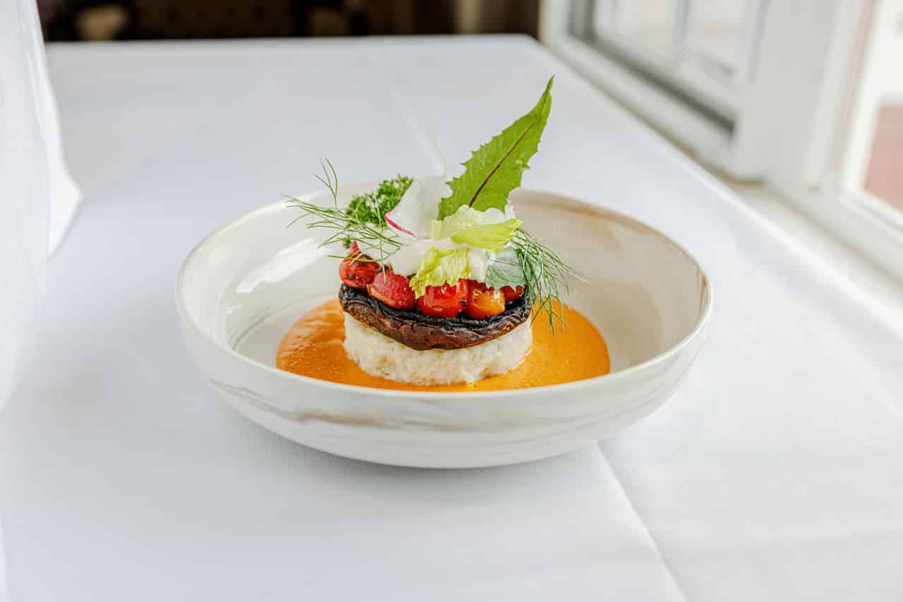 a photo of an elegant dining dish from Alma Via de San Camarillo's kitchen, garnished with greens and a tomato sauce.