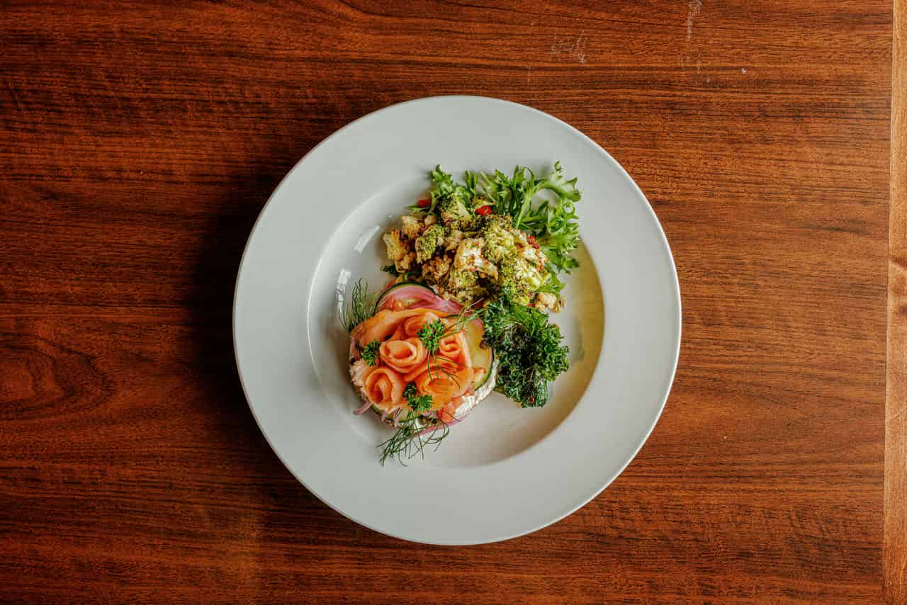 a photo of an elegant dining dish from Alma Via de San Rafael, A Salmon bagel with vegetables on the side.