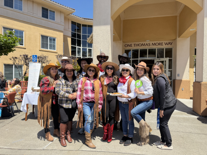 Executive Director Cleitus Jones and a group of people wearing cowboy hats and western-style clothing stand together outdoors in front of the AlmaVia of San Francisco building entrance
