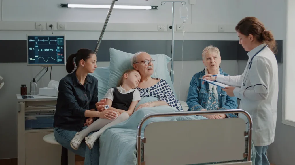A doctor discusses post-hospital care with a family gathered around an elderly man in a hospital bed.