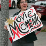 senior employee holds movie moments sign