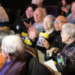 seniors watch intently and eat popcorn in a theatre